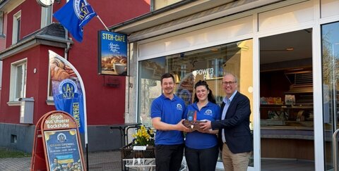 Zentrenmanager Stephan Frings (r., TROWISTA) überreicht Sonja (m.) und Sorrell (l.) Alex ein kleines Willkommensgeschenk vor der neuen Filiale der Bäckerei Alex in der Blücherstraße.   