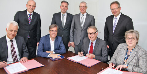Foto v .l.: Jürgen Krämer (Vorstand Raiffeisenbank Sankt Augustin), Ralf Löbach (Generalbevollmächtigter) , Prof. Dr. Martin Jonas (Aufsichtsratsvorsitzender), Holger Hürten (Vorstandsmitglied), Karl-Josef Schmitz (Vorstand Raiffeisenbank Sankt Augustin), Dr. Martin Schilling (Vorstandsvorsitzender), Andre Schmeis (Generalbevollmächtigter) und Barbara Welsch (Aufsichtsratsvorsitzende Raiffeisenbank Sankt Augustin) bei der Unterzeichnung des Verschmelzungsvertragsentwurfs